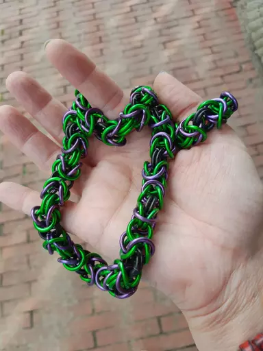 Une main tenant une chaine dite byzantine avec des anneaux vert, violet et noir.