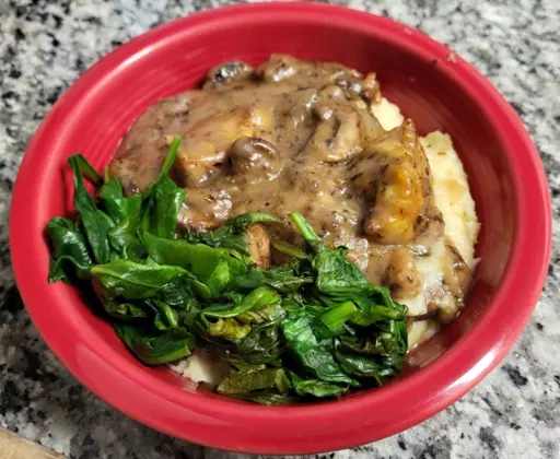 picture of a red bowl with cooked spinach on top of a dark gravy smothered over creamy polenta