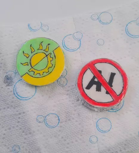 Two pins I made, one is showing a solarpunk symbol (yellow and green flag separated diagonally, like anarchist flags, with a half of a sun symbol, representing solar power, on the green side and a half of a gear symbol on the yellow side, representing technology) and the other one has "AI" written on it, crossed out with a red stroke