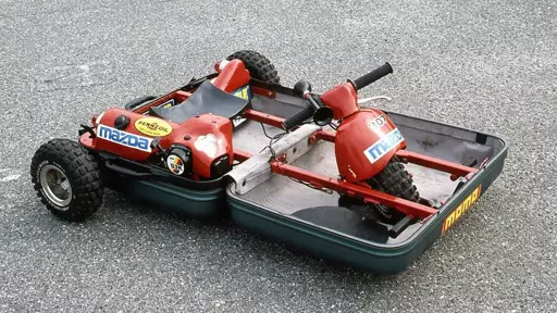 An open suitcase whose contents include a seat, engine, and steering column. The outside of the suitcase has two small rubber tire wheels in the rear near the seat. The third front wheel protrudes partially above a cutout in the front of the suitcase, directly under the steering column.