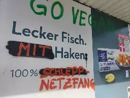 Fischstäbchen Werbeplakat von Frosta. Der Slogan "Lecker Fisch. Ohne Haken. 100% frei von Zusätzen." wurde teilweise mit Graffiti überschrieben zu: "Lecker Fisch. Mit Haken: 100% Schleppnetzfang."

Darüber in grüner Schrift: "Go vegan"