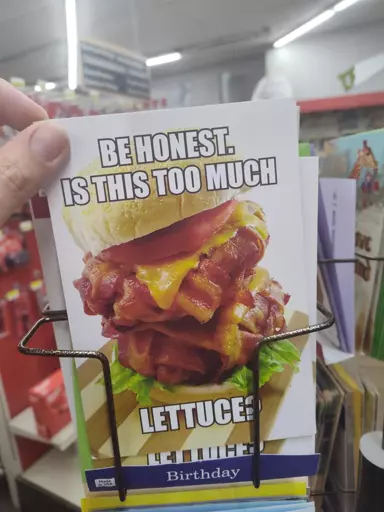 Hand holding a novelty card with a picture of a massive bacon cheeseburger. Card message reads, "Be honest, is this too much lettuce?"