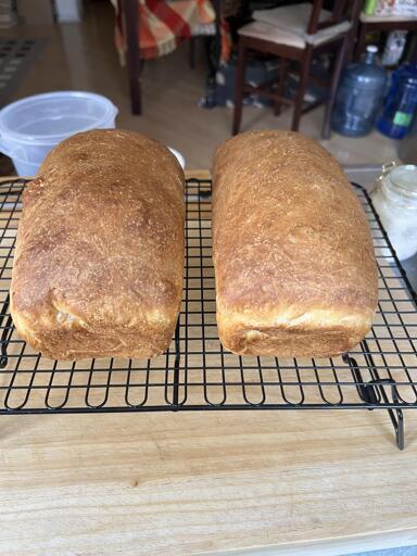 Two loaves of sourdough buttermilk sandwich bread sit on top of a wooden cutting board