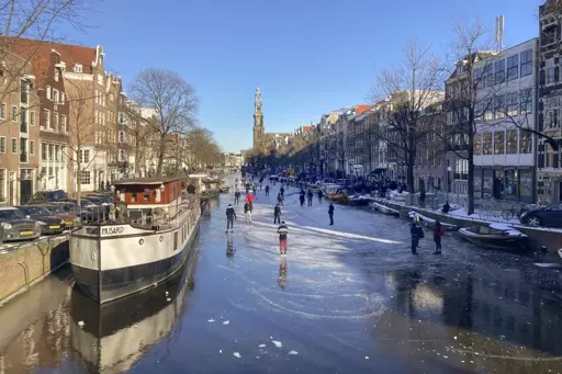 The Amsterdam canals frozen over, with people skating across it and between the boats moored to the sides.