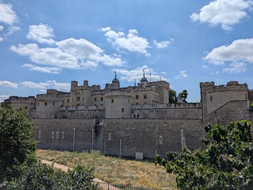 view of a castle with many walls and towers, blue sky partly cloudy, some trees on the sides