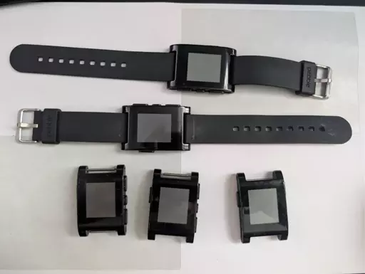 Five original Pebble watches on a desktop. Two of them have original straps, the other three have no straps.