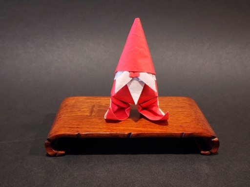 a photo of a Christmas gnome in origami. he's standing on a little wooden display.
